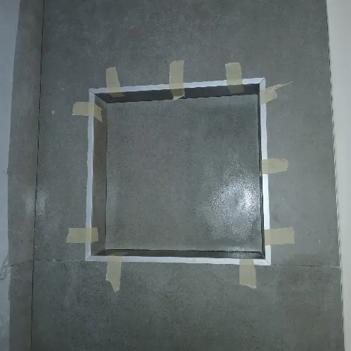 A square recess in a gray tiled wall is outlined with masking tape at the edges, possibly preparing for further work or installation.